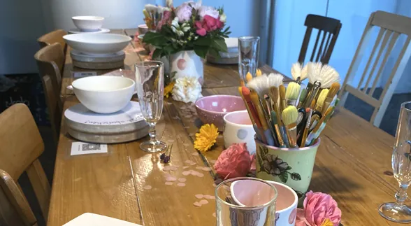 Gedeckter Tisch mit Keramik, Blumen und Pinseln